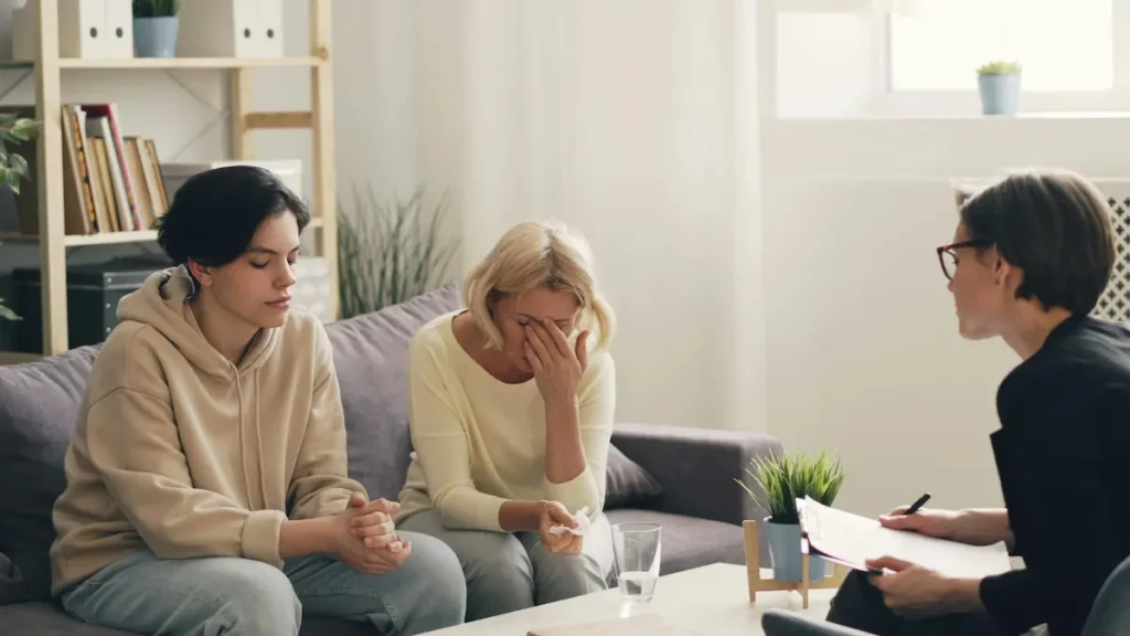 Two women receiving miscarriage counseling, with one visibly emotional and a counselor taking notes